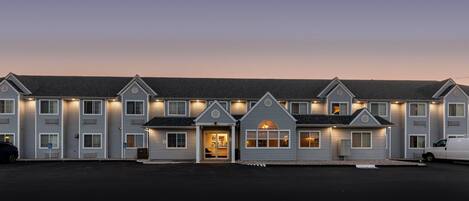 A multi-story hotel with a central entrance, multiple windows, and a parking area.
