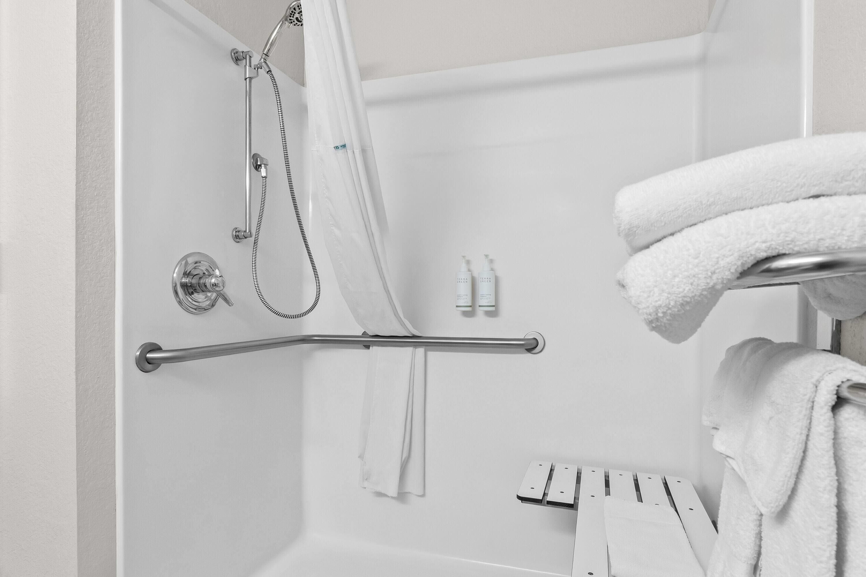 Ducha con cabezal de ducha de mano, puerta de cristal y toallero con toallas dobladas.