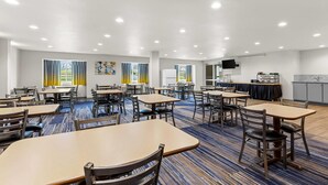 Een restaurantruimte in een hotel met tafels, stoelen, een keukenhoek en een flatscreen aan de muur.