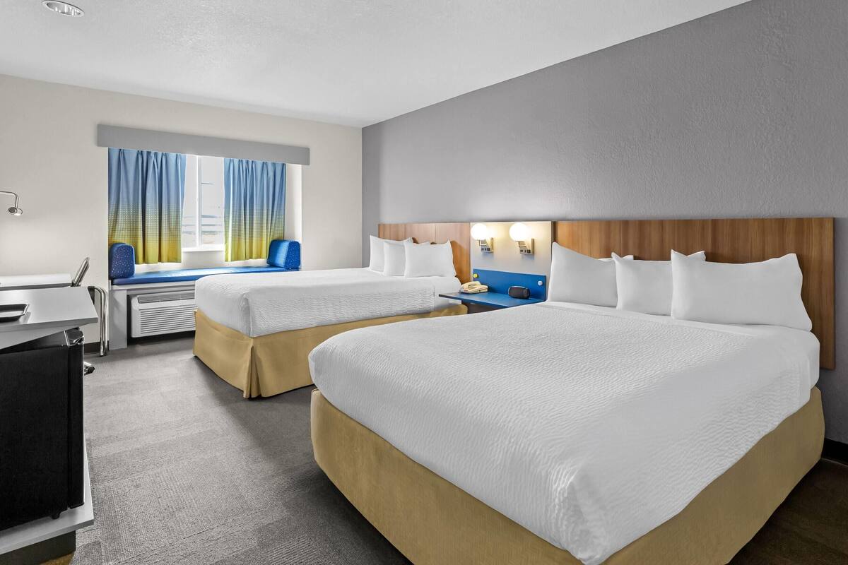Ein Hotelzimmer mit zwei Betten, einem Schreibtisch, einem Sessel und einem fensterbelagten Fenster.