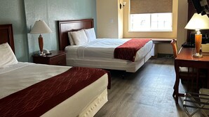 A hotel room with two beds, a desk with a lamp, a window with blinds, and a ceiling light.