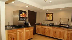 A modern kitchen with wooden cabinets, a stainless steel refrigerator, a coffee machine, and a fruit juice dispenser. - Expo Inn Hotel (Tulsa)