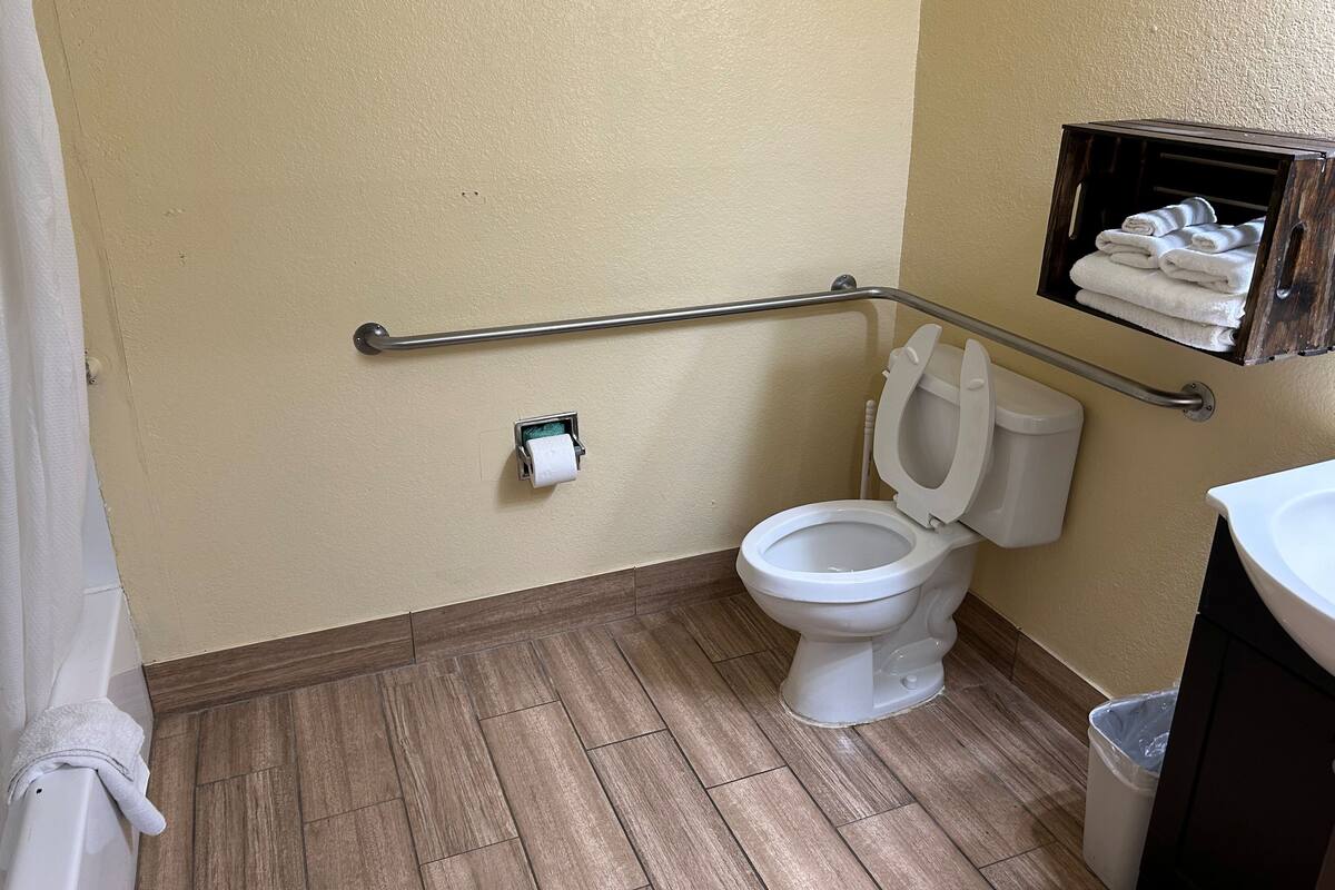 A bathroom with a toilet, a handrail, a towel rack, and a trash bin.