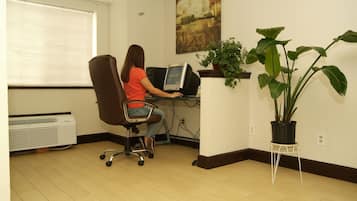 A person working at a desk in a room with a large window, a potted plant, and a painting on the wall.
