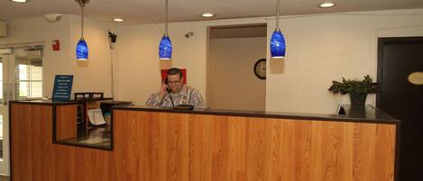 A reception desk with a wooden finish, a clock on the wall, and blue hanging pendant lights.