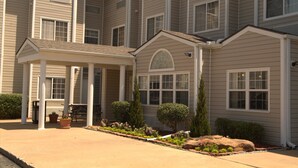 A multi-story residential building with a covered porch, potted plants, and a landscaped garden.
