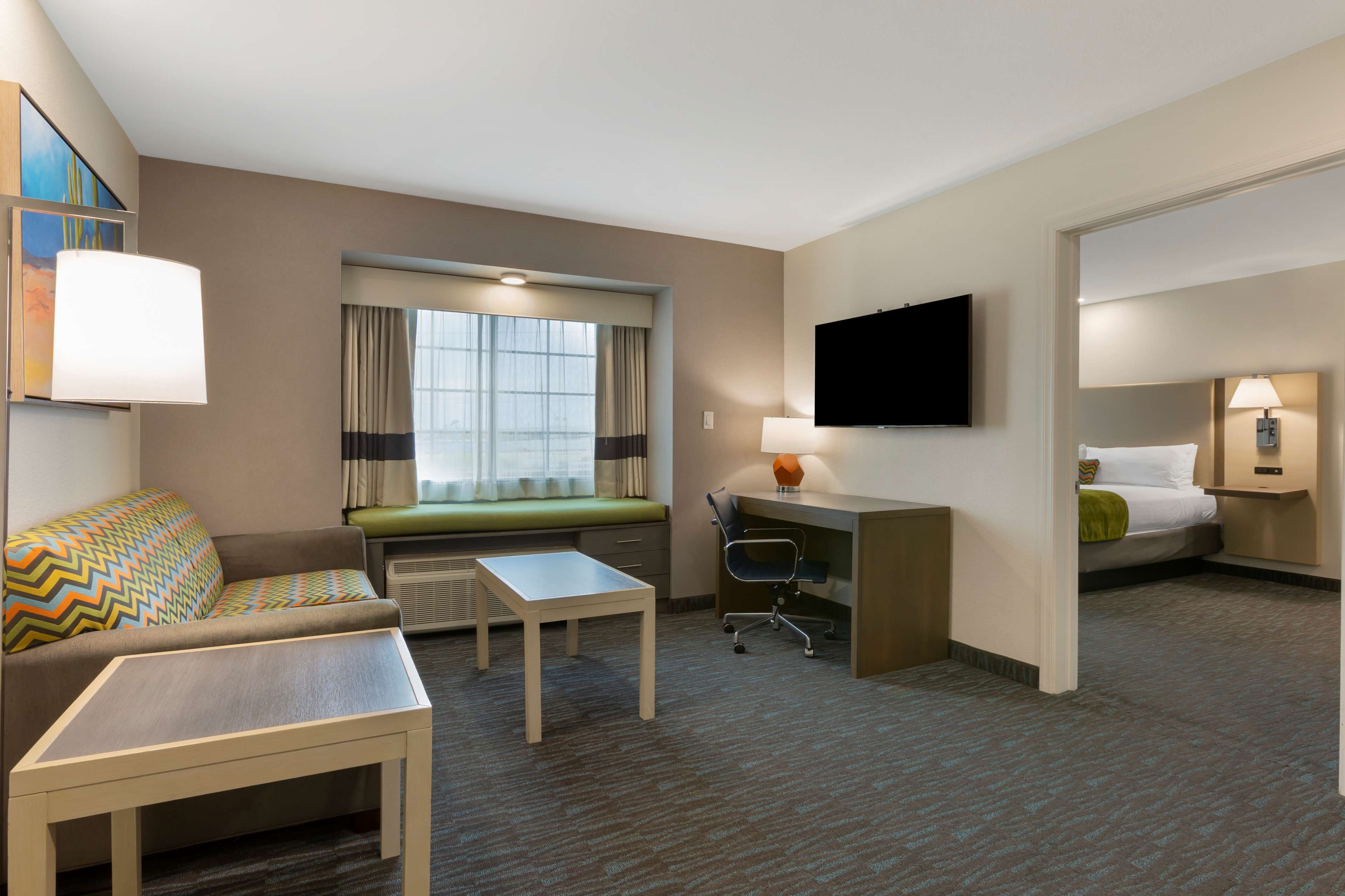 A hotel room with a sofa, a small table, a desk, a television, and a bed.