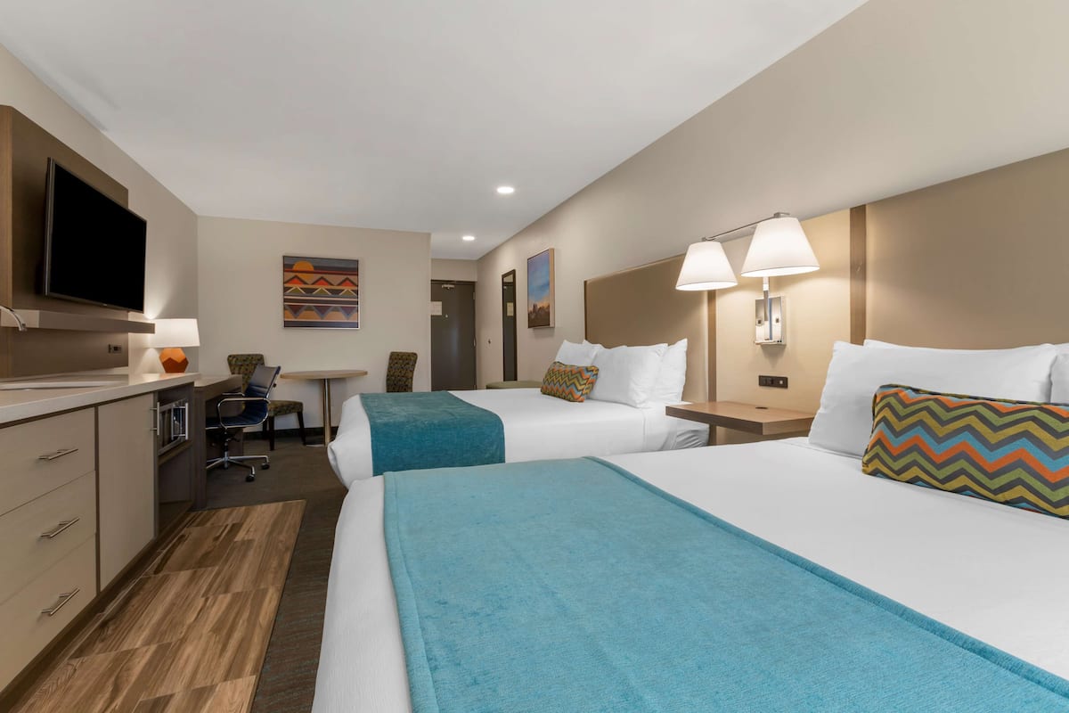 A hotel room with two beds, a desk, a TV, and a chair.