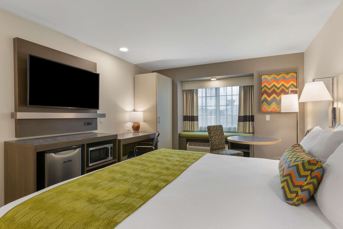 A hotel room with a bed, a desk, a television, a microwave, and a small dining table.