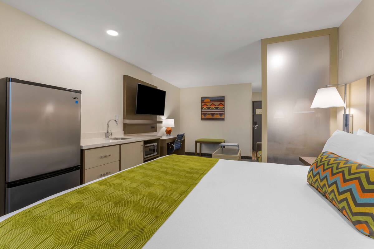A hotel room with a bed, a desk, a refrigerator, a television, and a wall-mounted lamp.
