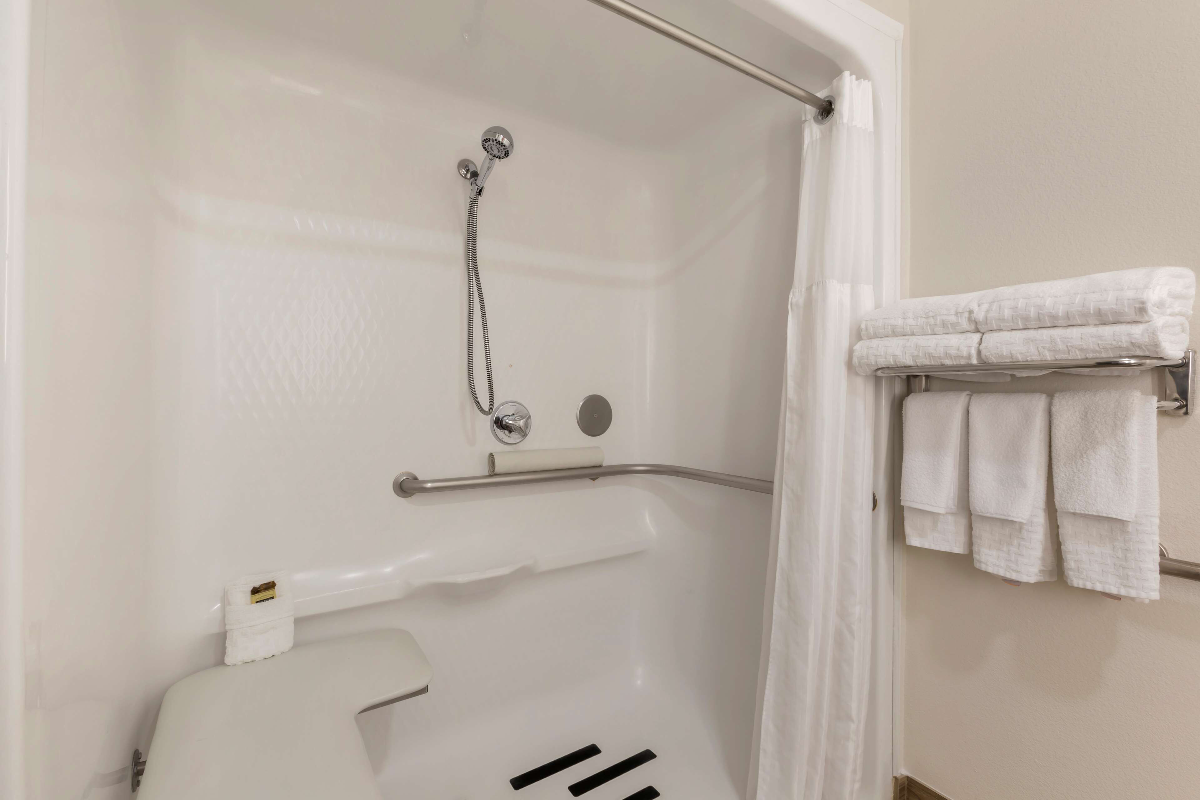 A shower area with a glass door, a towel rack with folded towels, and a toilet paper holder.