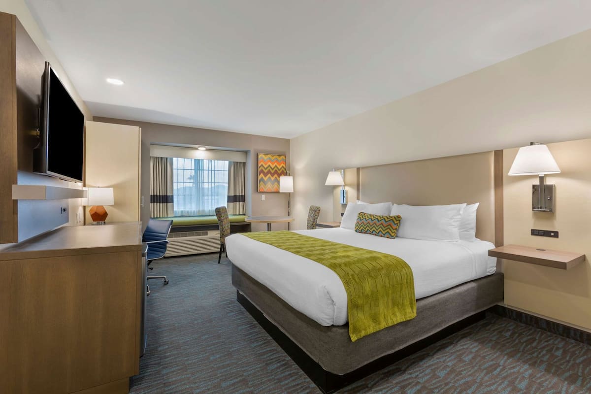 A hotel room with a bed, bedside tables, a desk, a chair, a TV, and a window with curtains.