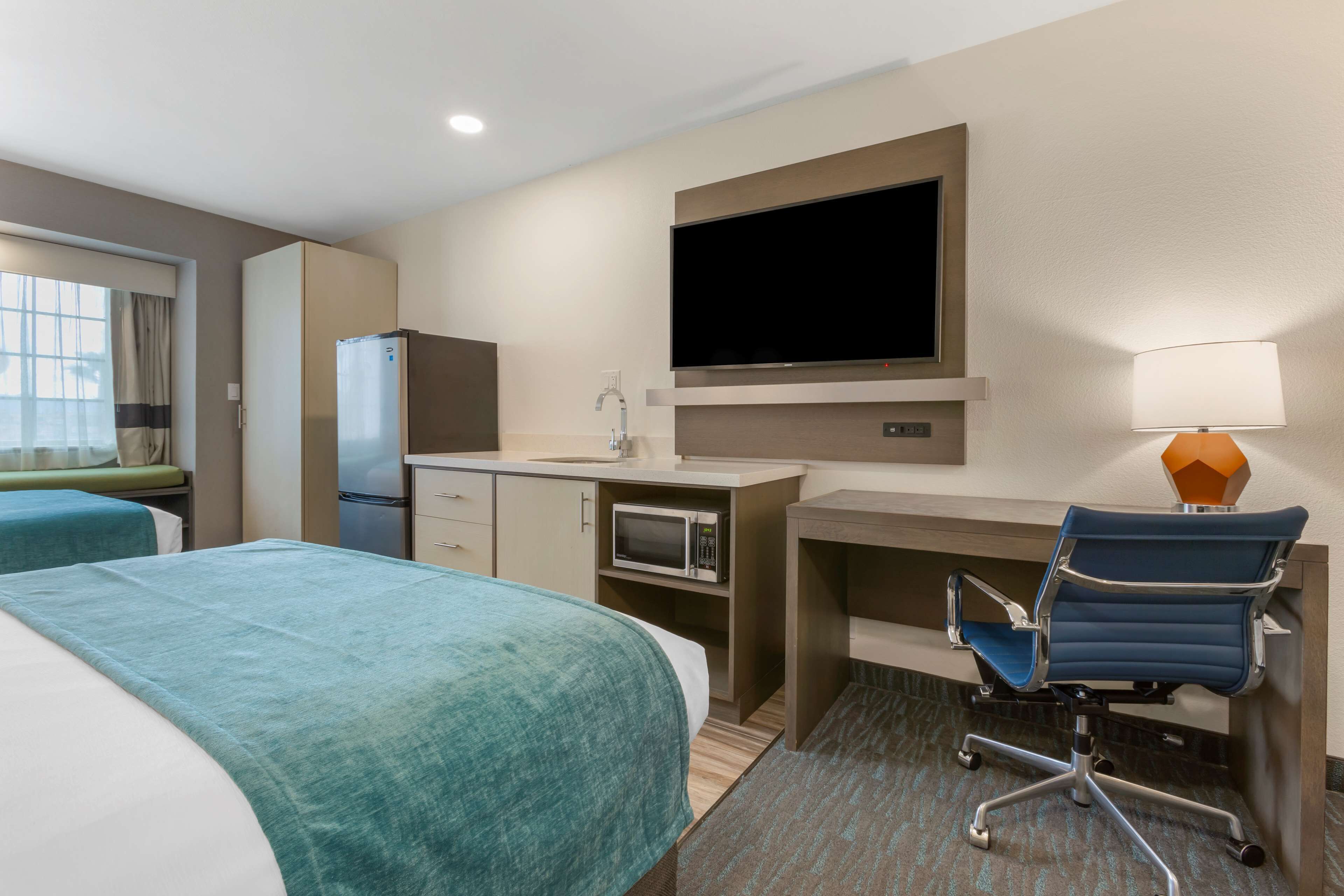 A hotel room with two beds, a desk, a TV, a microwave, a refrigerator, and a chair.