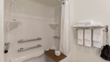 Un baño moderno con cabina de ducha, barras de apoyo, toallero y un pequeño estante de madera.