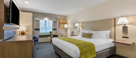 A hotel room with a large bed, a desk, a TV, and a window with curtains.