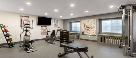 A gym with exercise equipment, a bench, a wall-mounted TV, and motivational posters.