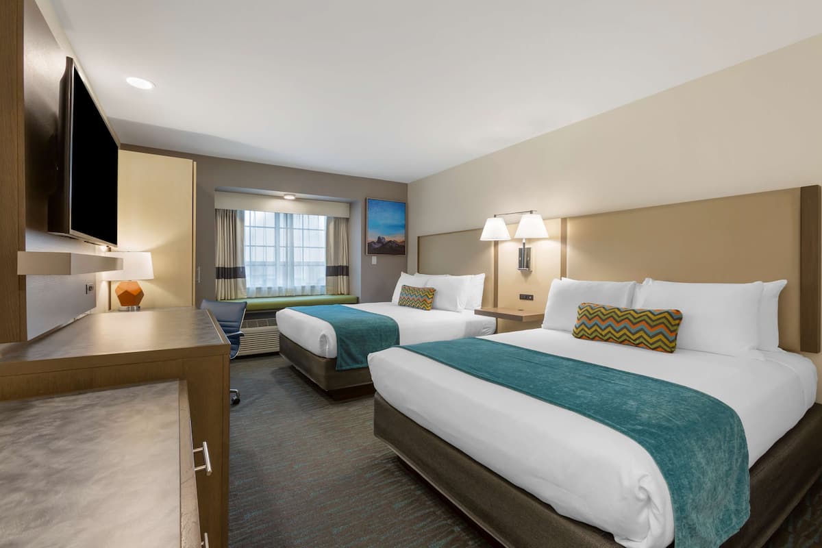 A hotel room with two beds, a desk, a television, and a window with curtains.