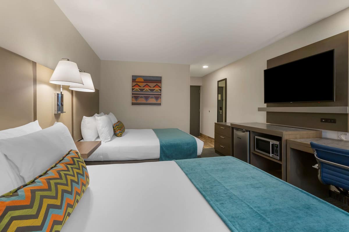 A hotel room with two beds, a desk, a television, and a microwave.