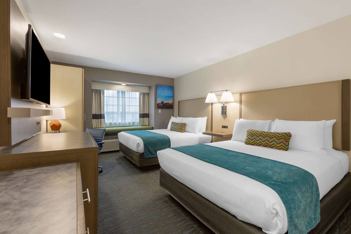 A hotel room with two beds, a desk, a TV, and a window with curtains.