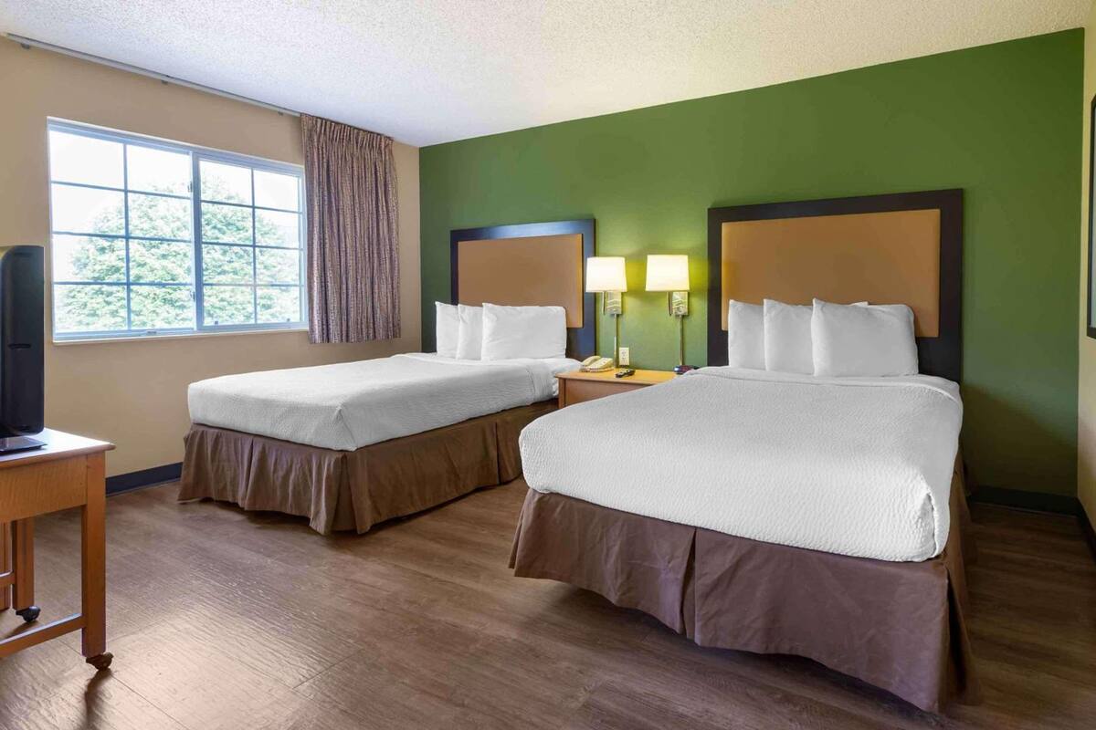 Habitación de hotel con dos camas, un ventanal grande, televisión y escritorio.