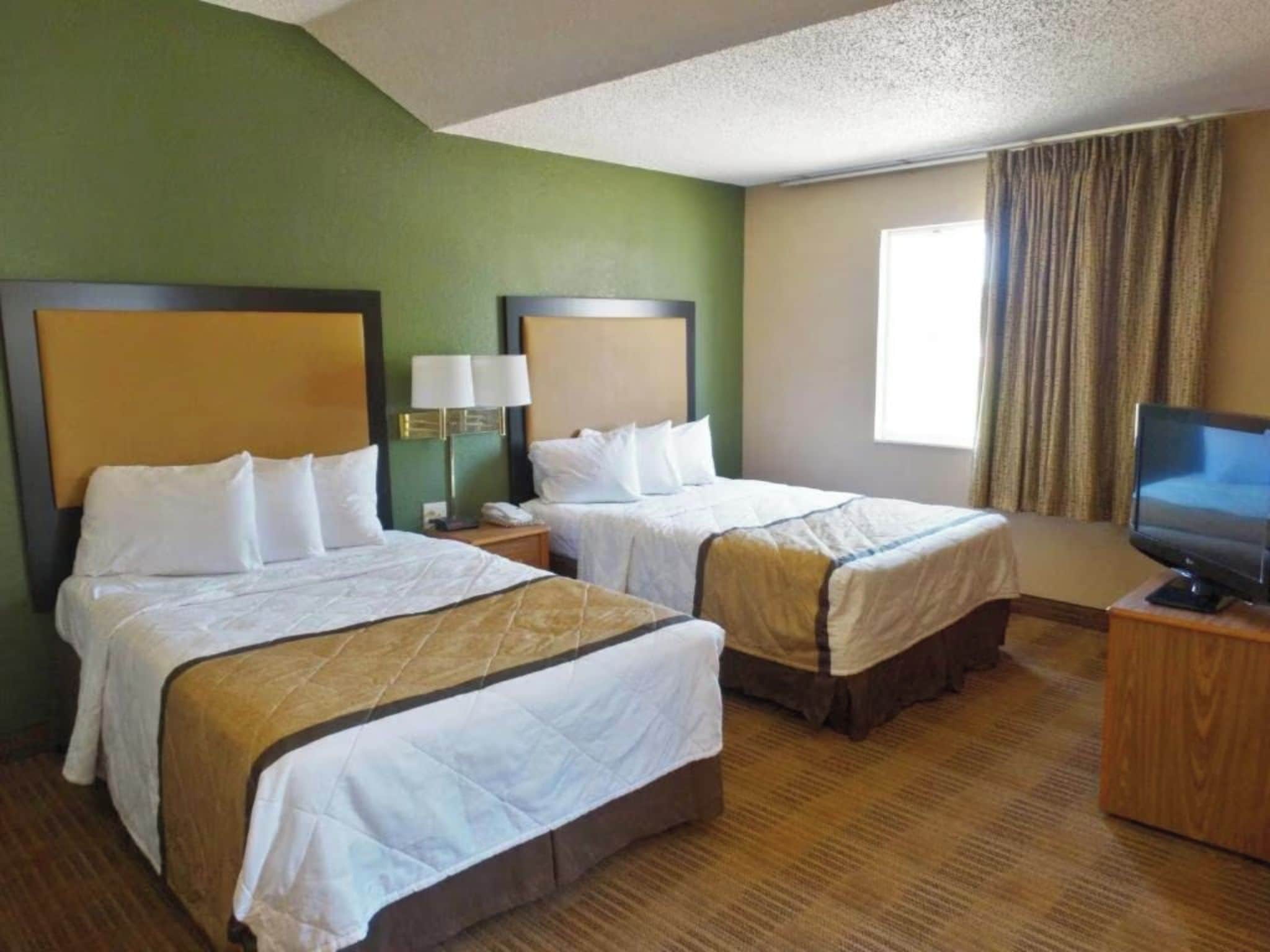 A hotel room with two beds, a television on a wooden stand, and a window with curtains.
