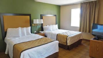 A hotel room with two beds, a television on a wooden stand, and a window with curtains.
