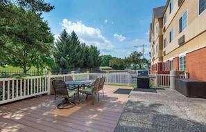 An outdoor patio with a table and chairs, a grill, and a building with windows. - Studio 6 Corporate Extended Stay Philadelphia Malvern Swedesford Rd. PA (Malvern)