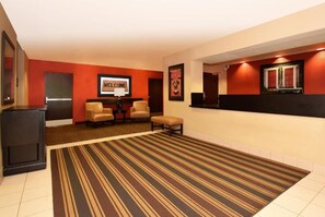 A hotel lobby with a reception desk, two armchairs, a bench, and a striped carpet. - Studio 6 Corporate Extended Stay Philadelphia Malvern Swedesford Rd. PA (Malvern)