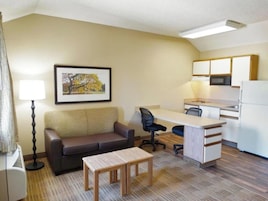 Habitación de hotel compacta con sofá, una mesita pequeña, escritorio con silla, kitchenette y un cuadro en la pared.