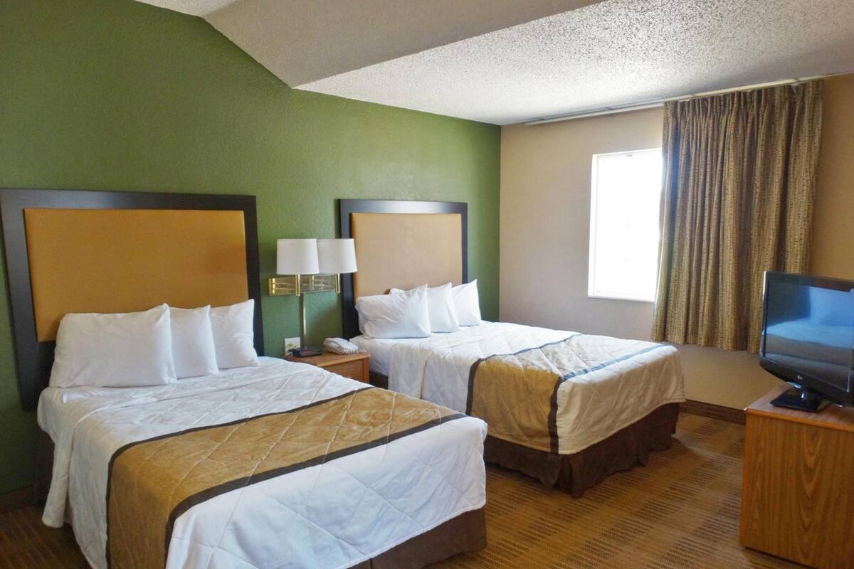 A hotel room with two beds, a television, and a window with curtains.