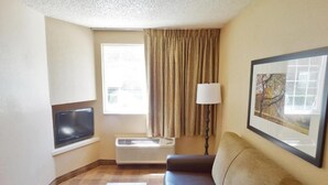 Habitación de hotel con sofá, una mesita, televisor, ventana con cortinas y un cuadro en la pared.