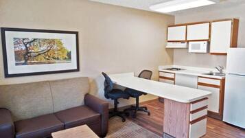 A compact living space with a kitchenette, a sofa, a small table, and a framed picture on the wall.