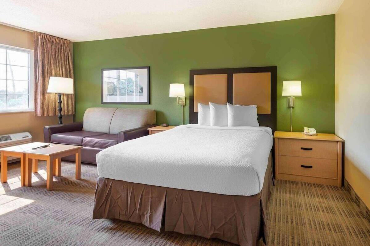 A hotel room with a large bed, a sofa, a desk, and two bedside tables with lamps.