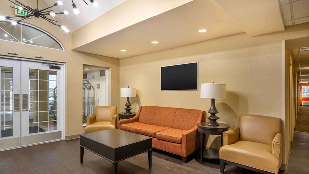 A lobby with a sofa, chairs, a coffee table, and a TV on the wall. - Extended Stay America Suites - Charleston - Airport (North Charleston)