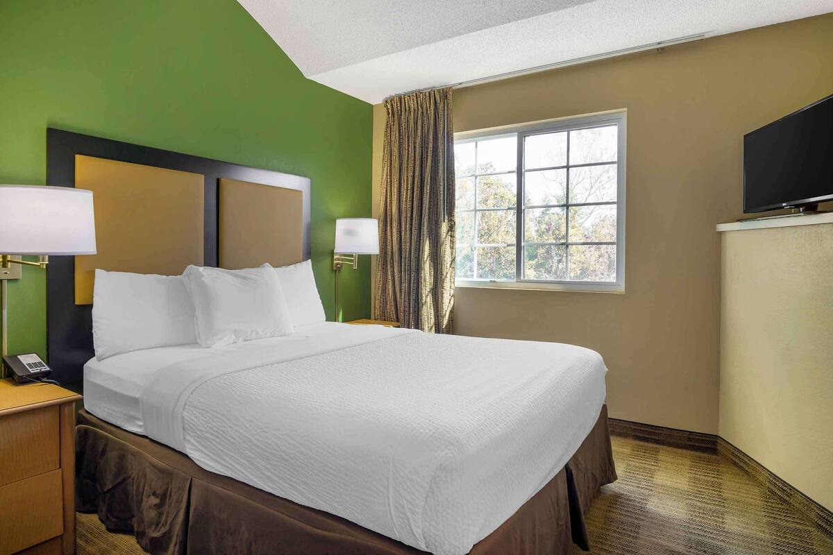 A hotel room with a large bed, two bedside lamps, a flat-screen TV, and a window with curtains.
