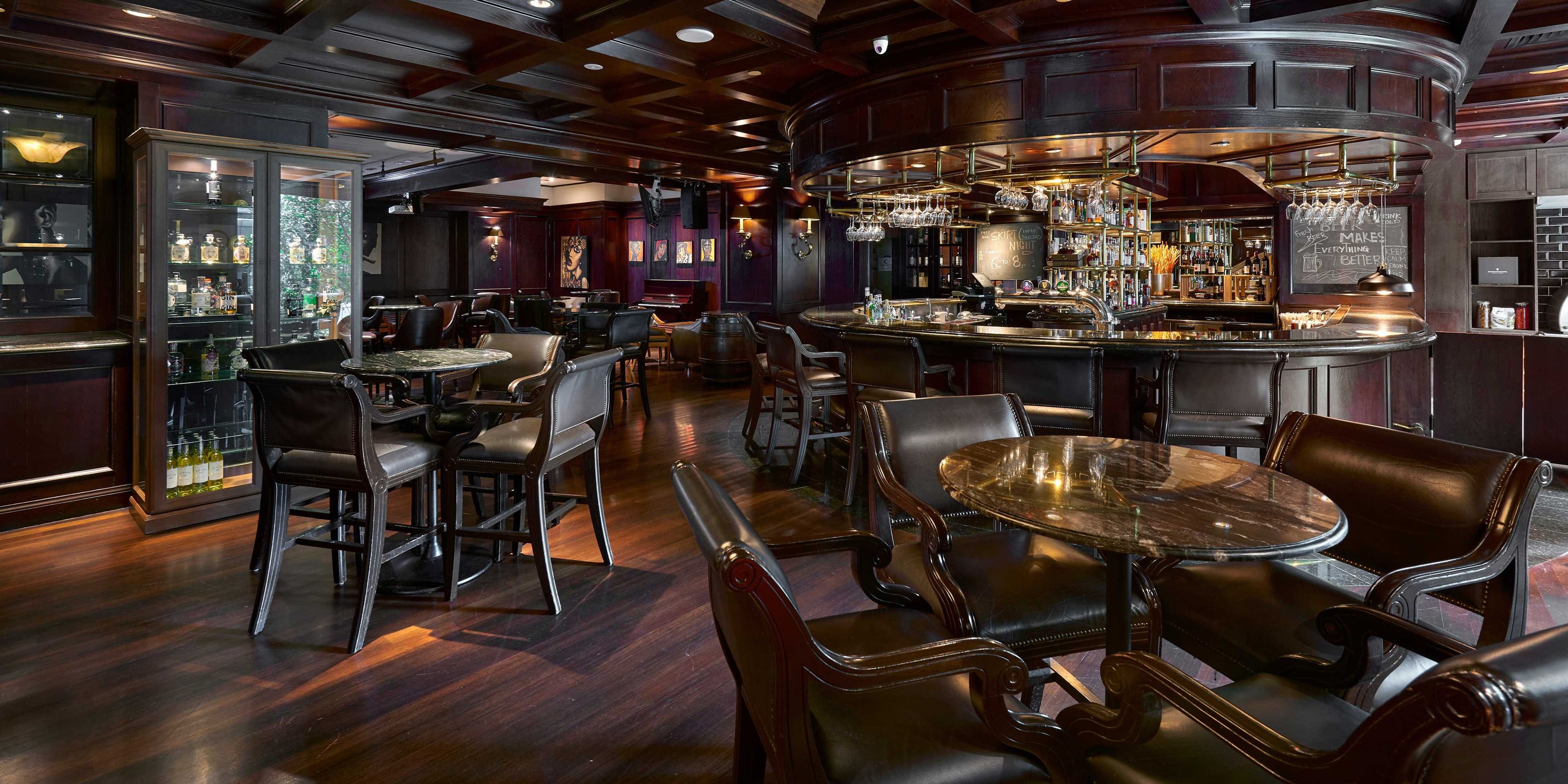 A bar area with wooden furniture, a piano, and a variety of bottles.