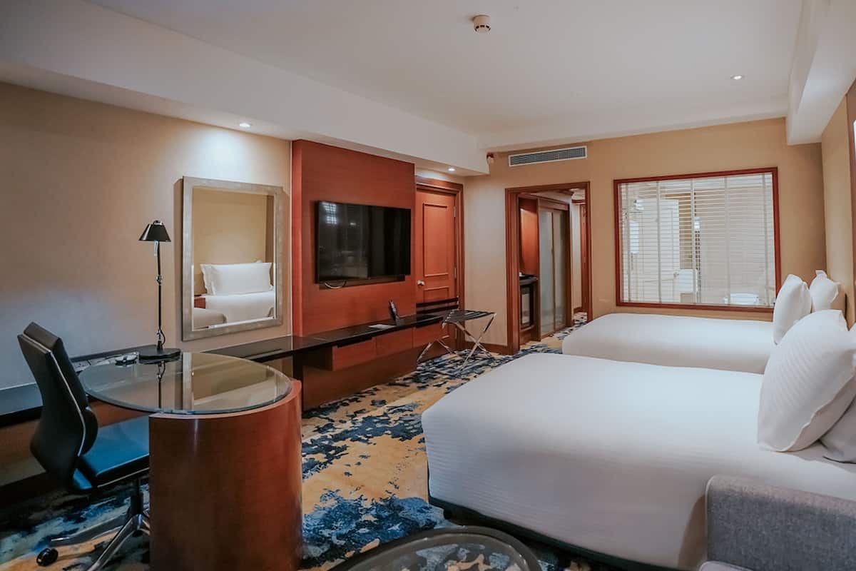 A hotel room with a bed, a desk, a chair, a TV, and a window with blinds.