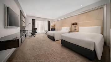 A hotel room with two beds, a desk with a computer, a TV, and a large window with curtains.