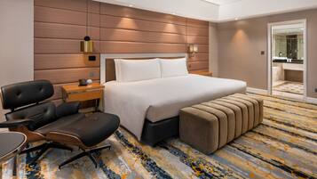A hotel room with a large bed, a desk with a chair, a bedside table, and a bathroom visible through an open door.