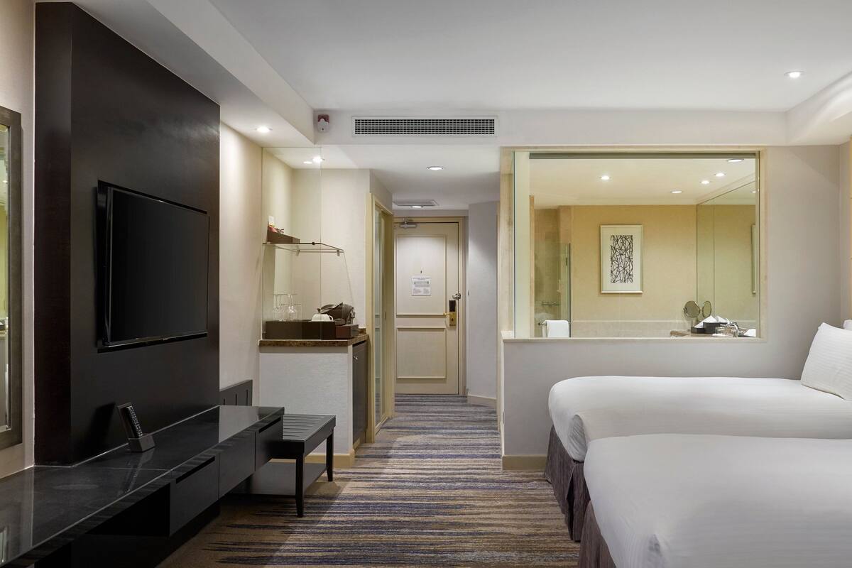 A hotel room with a TV, a desk with a chair, a bed, a bathroom with a mirror, and a carpeted floor.