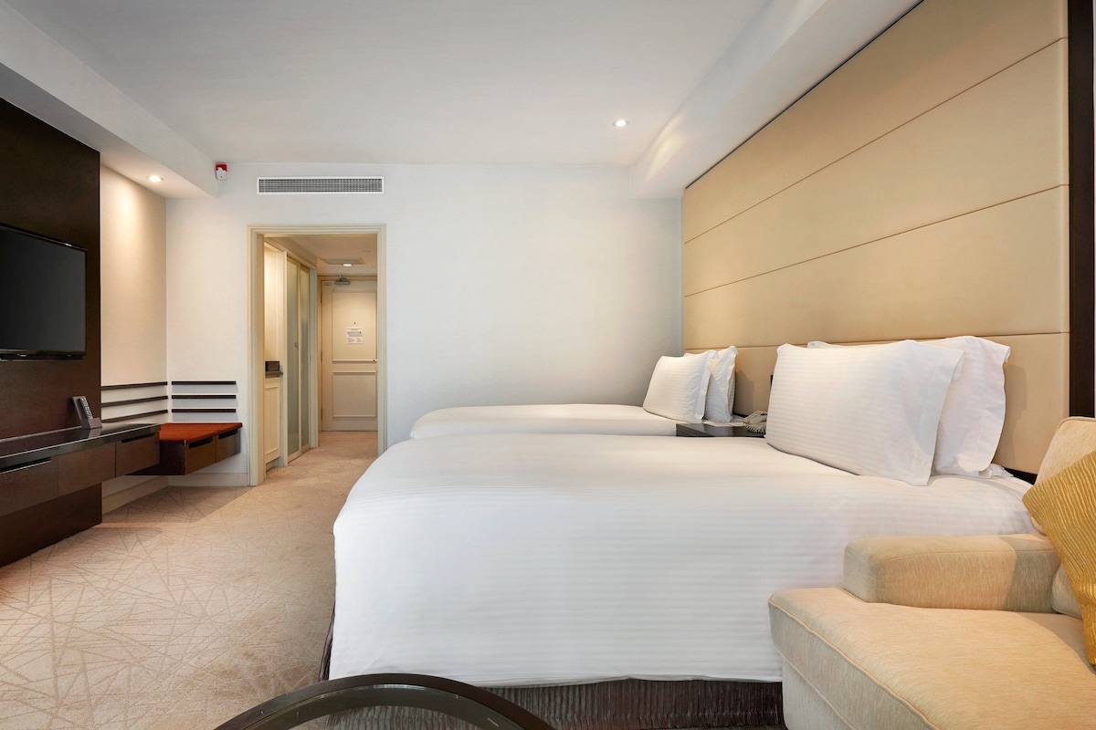 A hotel room with a large bed, a TV mounted on the wall, a desk with a chair, and a sofa.