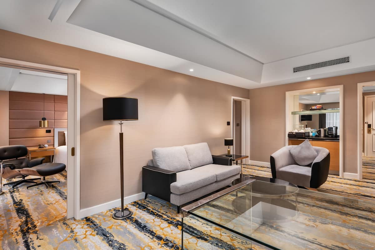 A modern hotel room with a sofa, armchair, and a glass coffee table.