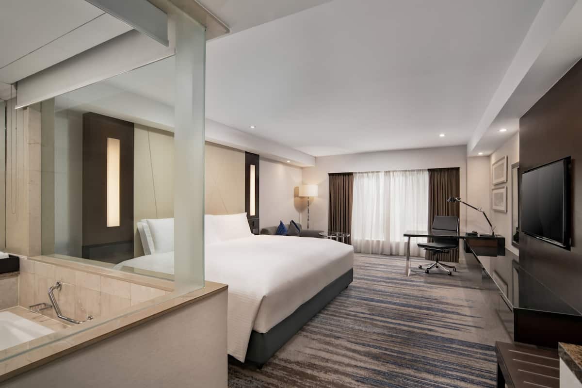 A hotel room with a large bed, a desk, a TV, and a bathroom with a glass-enclosed shower.