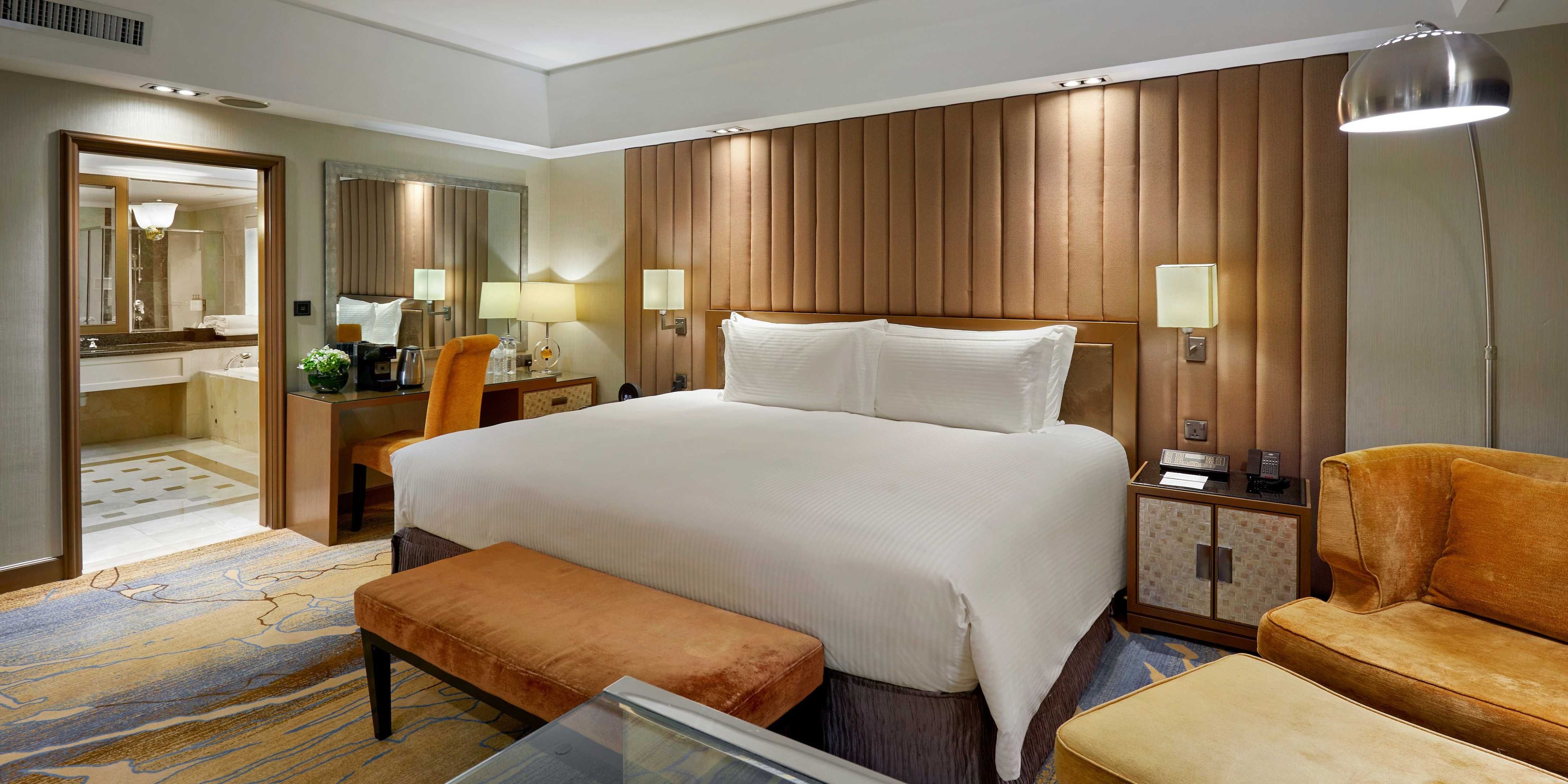 Una habitación de hotel con una cama grande, un escritorio con una silla, un sofá, una mesita, un espejo y una lámpara.