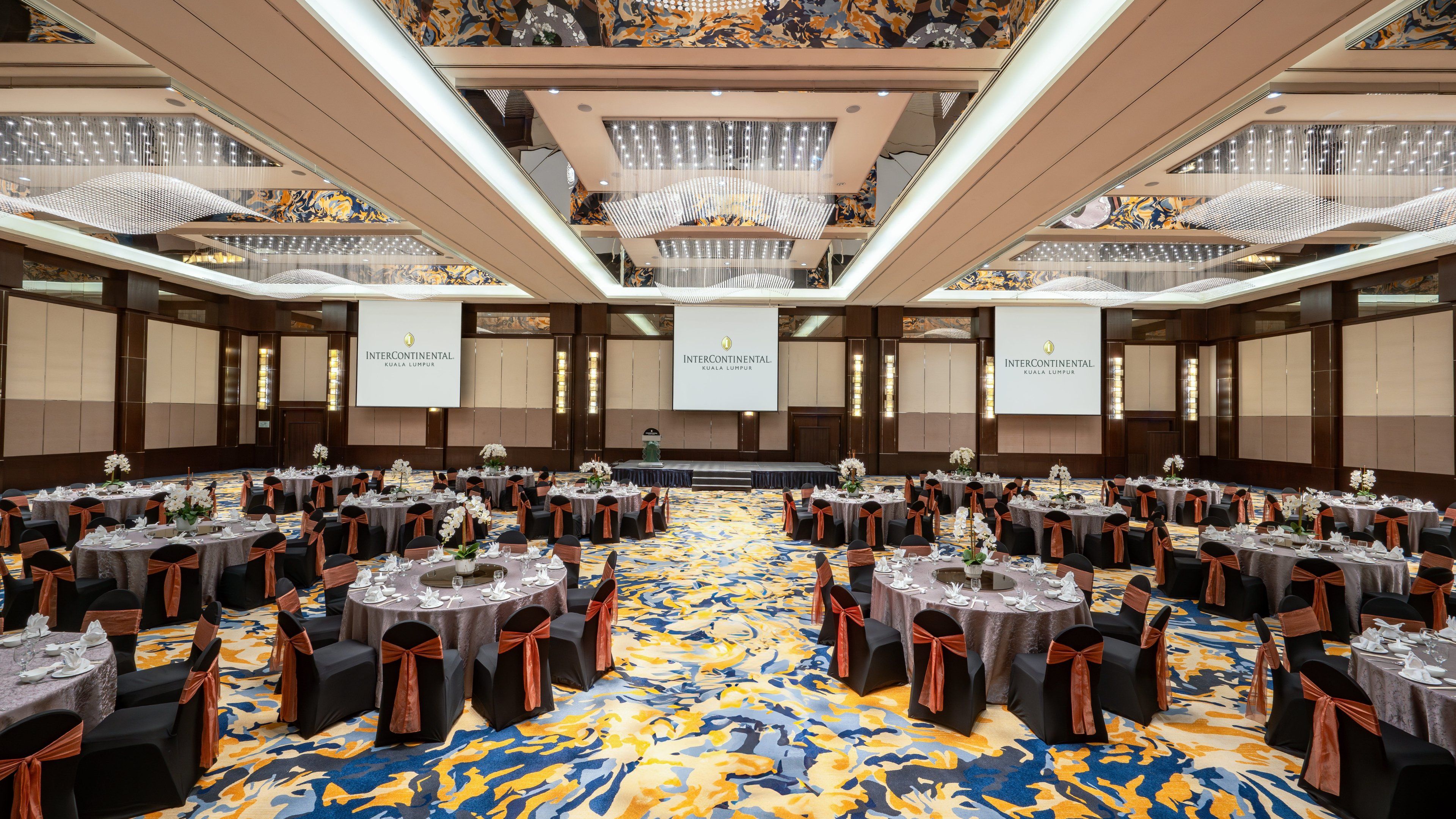 Een ruime congreszaal met meerdere ronde tafels, elk voorzien van stoelen en decoraties, in een hotel.