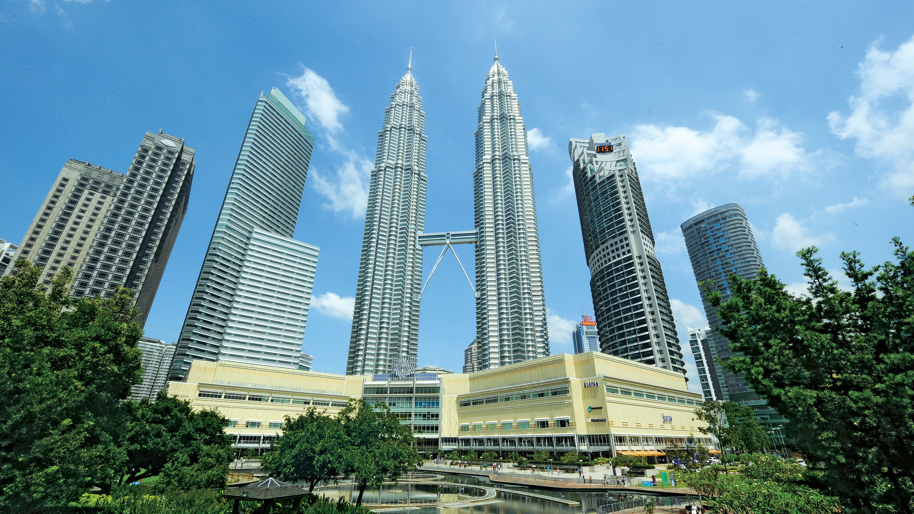 A cluster of high-rise buildings with a prominent central tower, surrounded by greenery and a body of water.