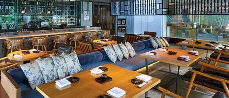 Un restaurant moderne doté d’un bar, de différents espaces pour s’asseoir et offrant une vue grâce à de grandes fenêtres.