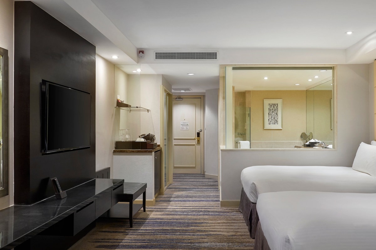 A hotel room with a TV, a desk with a chair, a bed, a bathroom with a mirror, and a carpeted floor.