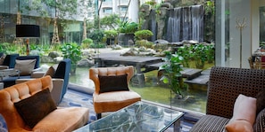 Un vestíbulo de hotel con asientos, una mesa de vidrio, una cascada y plantas de interior.