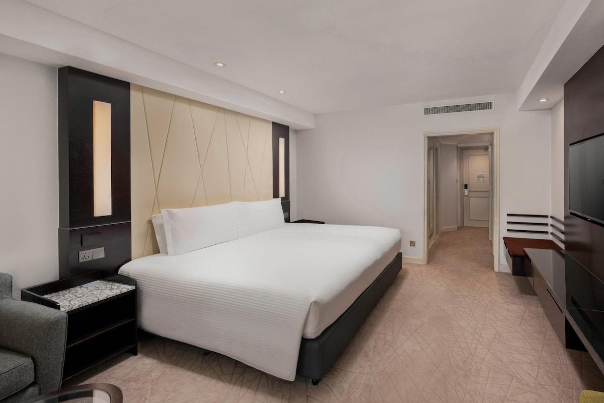 A modern hotel room with a large bed, a TV, a desk, and a chair.